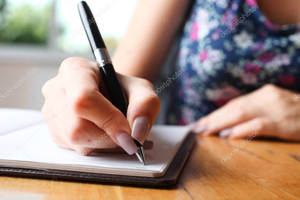Woman writes in notebook at table. Concept writer.