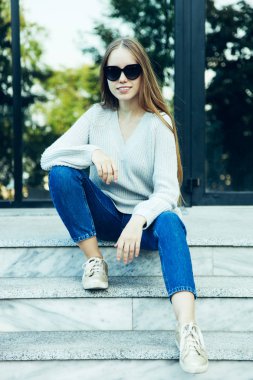 Kız sıcak kazak ve kot merdiven üstünde oturuyor. Kavram sonbahar kıyafetleri.