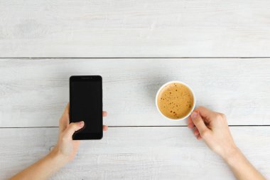 Smartphone el ve ahşap arka plan üzerinde kahve. Üstten görünüm.