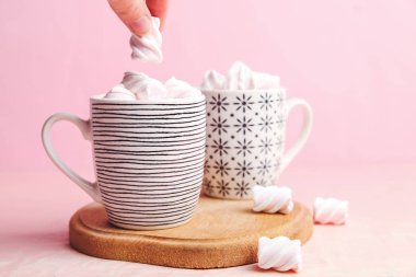 Pembe bir arka plan üzerinde ahşap tahta üzerinde marshmallows fincanla.