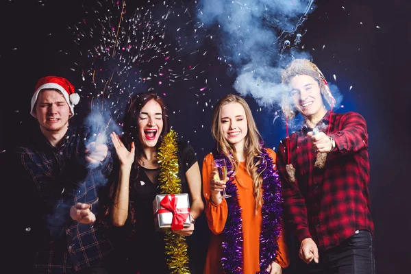 Cheerful company of friends, firecrackers and confetti on black background. Concept New Year.