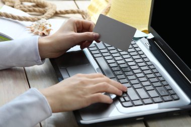 Yaz tatili, turizm ve tatil. Kadın kredi kartı elinde tutan ve arkasında ahşap arka plan üstünde laptop Internet üzerinden online satın alma işlemi yaptığı. Yan görünüm.