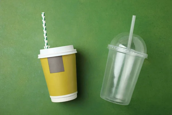 Yellow and transparent plastic disposable cups with cocktail tubes on green background. Top view.