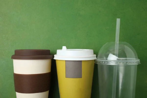 Three different plastic disposable cups on green background. Top view, copy space.