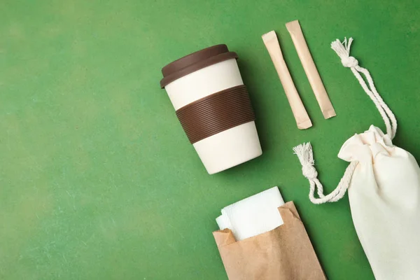 Eco bag, reusable bamboo cup and craft packages on green background. Concept ecology conservation. Flat lay, copy space. Environmentally friendly materials.