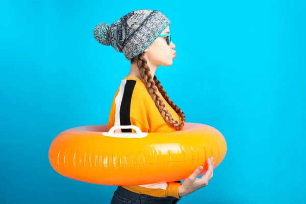 女孩在冬天衣服与充气橙色圈子游泳在蓝色背景 概念暑假 — 图库照片