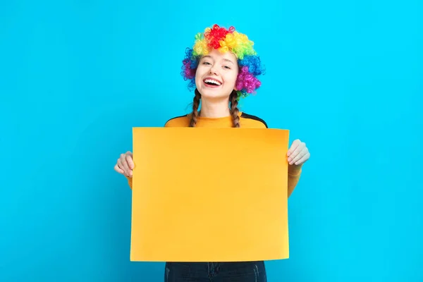 微笑的开朗的女孩小丑与蓝色背景上的大黄色纸纸 复制空间 — 图库照片