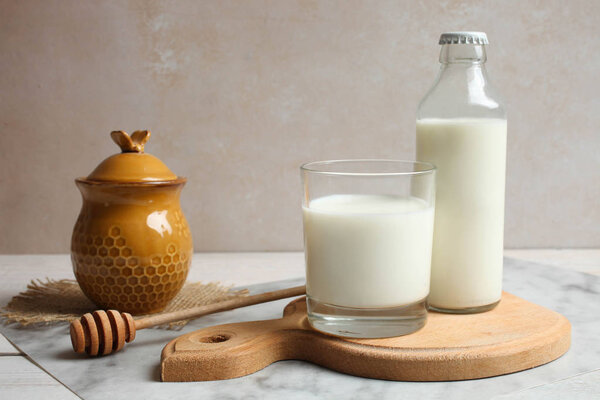 Jar of honey and glass of milk on wooden cutting board on table on neutral background. Copy space.