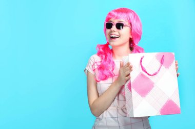 Elbise alışveriş çantası üzerinde mavi arka plan ile parlak pembe saçlı güzel gülümseyen kız. Konsept satış, alışveriş.