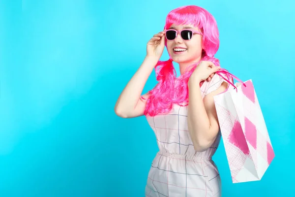 美丽的微笑的女孩与明亮的粉红色头发在礼服与购物袋在蓝色背景 概念销售 — 图库照片