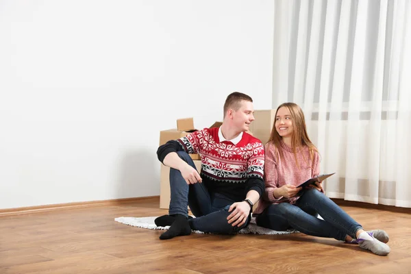 Girl and guy, young happy couple in love are sitting on wooden floor near boxes in new apartment.  Copy space. Concept buying apartment, relocation.
