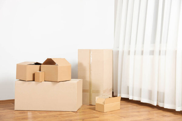 Stack of cardboard boxes stand in empty room on wooden floor, against the wall. Copy space. Concept moving to new apartment.