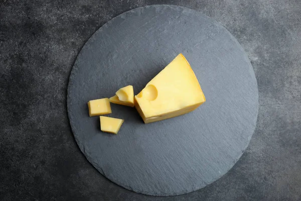 Hard sliced yellow Maasdam cheese slate blackboard on black background. Concept serving cheese. Top view, copy space.