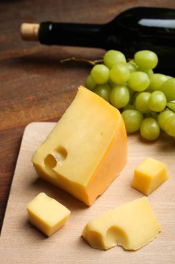 Sert ahşap zemin üzerinde kesme tahtası, beyaz üzüm ve şarap sarı Maasdam peyniri dilimlenir. Kavram hizmet peynir.
