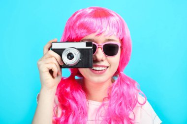 Mavi arka plan üzerinde eski retro kamera ile parlak pembe saçlı güzel gülümseyen kız.