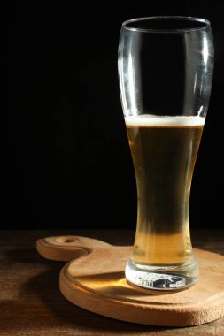 Cam kadeh içinde karanlık siyah arka plan üzerine ahşap kesme tahtası üzerinde hafif bira. Kavram alkol.