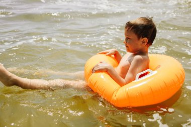 Çocuk parlak turuncu şişme daire ile denizde yüzer