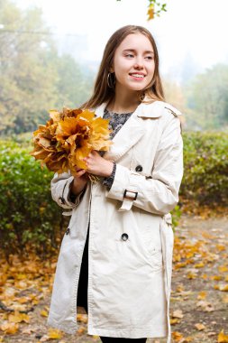 Kız sonbahar yaprakları buketiyle parkta yürür. 