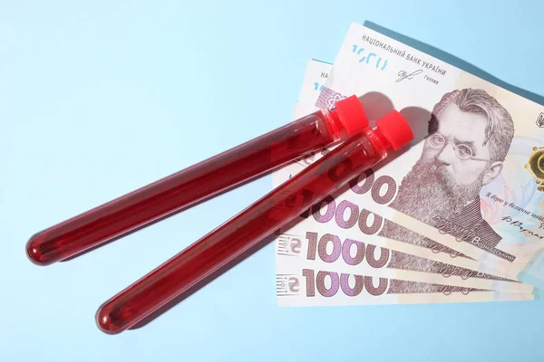 Test tubes with blood and money against blue background. Concept expensive analyzes.