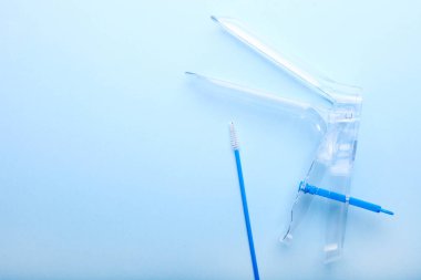 Tek kullanımlık jinekolojik spekulum ve mavi arka planda fırça..