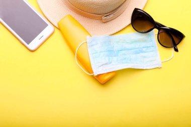 Plaj aksesuarları, akıllı telefon ve sarı arka planda tıbbi maske. İyi yolculuklar..