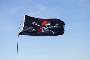 Siyah korsan bayrağı Jolly Roger mavi gökyüzünde dalgalanıyor.