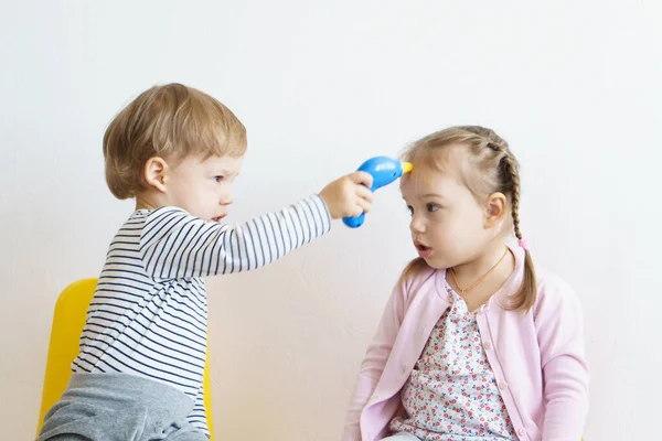 Duas crianças brincam de médico no berçário. Irmão de óculos amarelos trata sua irmã, jogando dentista, otorrinolaringologista, oftalmologista, medição de temperatura. Jogos de interpretação de papéis para crianças, o desenvolvimento — Fotografia de Stock