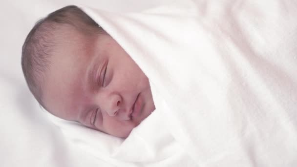 Childhood, infancy, parenthood, motherhood concept - close-up portrait of a newborn baby lying on a white beige bed wrapped in a diaper. Baby wakes up opens his eyes and sticks out his tongue. — Stock Video