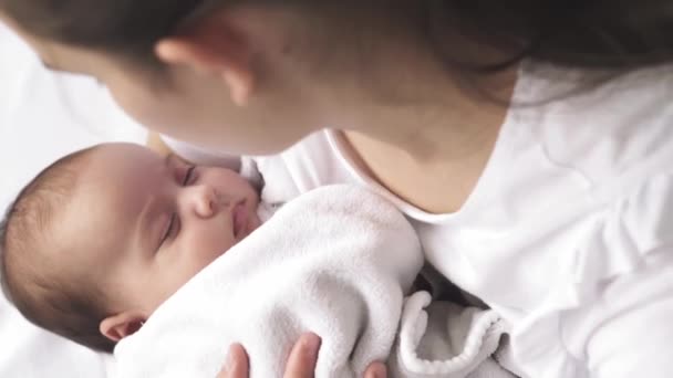 Bebé, maternidad, desarrollo, infancia, pediatría, medicina y concepto de salud - madre joven de cerca vestida de blanco sostiene en sus brazos al bebé recién nacido envuelto en caricias de manta y arrullos niño . — Vídeo de stock