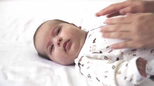 Infant, motherhood, development, childhood, training, pediatrics, medicine and health concept - close-up naked newborn lies wakes up mom puts baby in bodysuit. on white background. — Stock Video