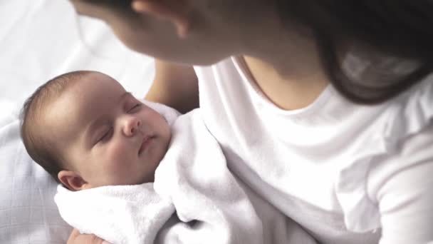 Infant, motherhood, development, childhood, pediatrics, medicine and health concept - close-up young mother dressed in white holds in her arms newborn baby wrapped in blanket caresses and lulls child. — Stock Video