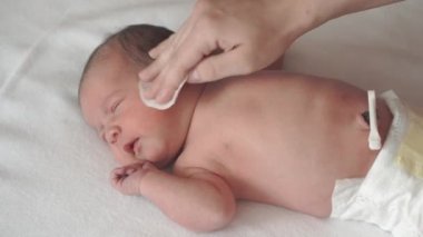 bebek bezi, çocukluk, annelik, hijyen, ilaç ve sağlık konsepti - kadın anneler yeni doğmuş çıplak bebeğin yüzünü pamuk bezle siliyor ve sırtında tıbbi klipsle klempler takıyor.
