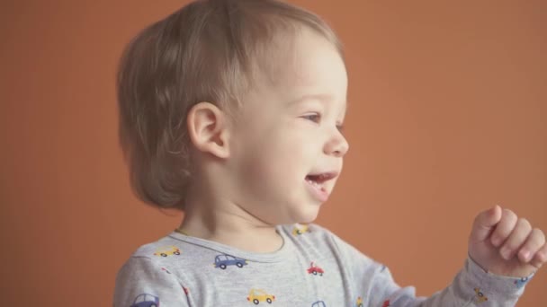 Children, celebration, birthday, games concept - close-up little 2 years blond-haired boy in gray bodysuit smiling dancing looking at camera and showing different emotions on orange solid background. — Stock Video