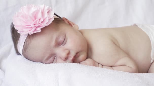 Infancy, childhood, development, medicine and health concept - close-up face of a newborn naked sleeping baby girl lying on her stomach with a bandage and a flower on her head on a pink background. — Stock Video