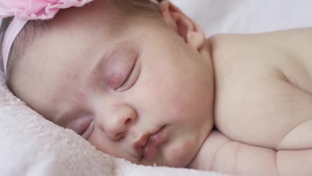 Kindertijd, kindertijd, ontwikkeling, geneeskunde en gezondheid concept - close-up gezicht van een pasgeboren naakt slapende baby meisje liggend op haar buik met een verband en een bloem op haar hoofd op een roze achtergrond. — Stockvideo