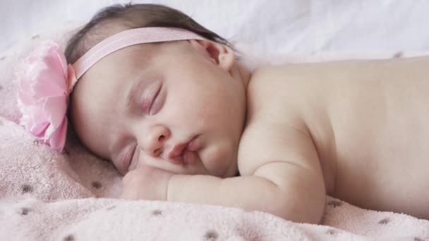 Kindertijd, kindertijd, ontwikkeling, geneeskunde en gezondheid concept - close-up gezicht van een pasgeboren naakt slapende baby meisje liggend op haar buik met een verband en een bloem op haar hoofd op een roze achtergrond. — Stockvideo