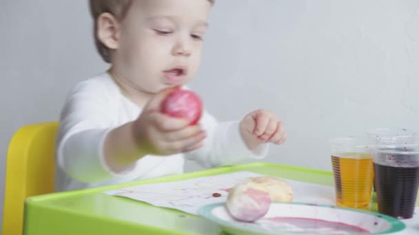 Um menino loiro pinta ovos de galinha por coloração de alimentos. Preparação para a Páscoa. Pintura com as mãos dentro de casa. Desenvolvimento criativo para crianças menores de 3 anos. Educação, desenho em casa durante — Vídeo de Stock
