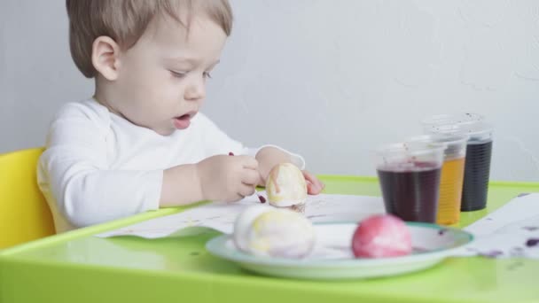 一人の金髪の少年は食べ物の着色料で鶏の卵をペイントする。イースターの準備。手で屋内で絵を描く。3歳未満の子供のための創造的な開発。教育、家庭での描画中に — ストック動画