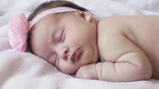 Infancy, childhood, development, medicine and health concept - close-up face of a newborn naked sleeping baby girl lying on her stomach with a bandage and a flower on her head on a pink background. — Stock Video