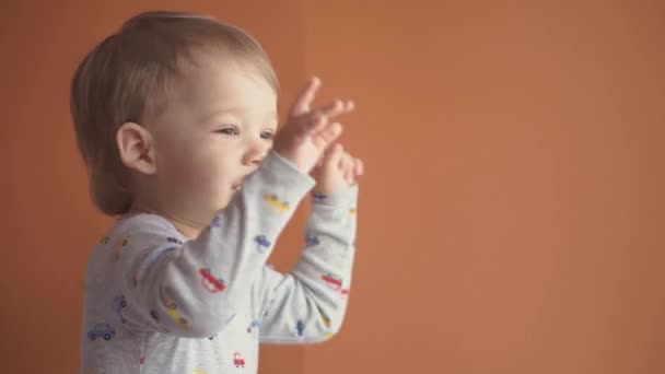 Bambini, festa, compleanno, concetto di giochi - primo piano piccolo 2 anni ragazzo biondo in body grigio sorridente che balla guardando la fotocamera e mostrando diverse emozioni su sfondo solido arancione. — Video Stock