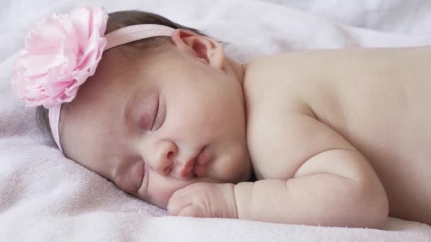 La infancia, la infancia, el desarrollo, la medicina y el concepto de salud: primer plano de la cara de una niña recién nacida que duerme desnuda acostada boca abajo con un vendaje y una flor en la cabeza sobre un fondo rosa. — Vídeo de stock
