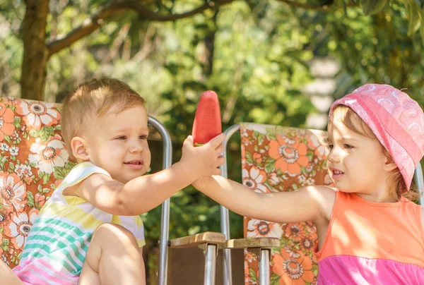 Vacation, summer, village, vacation, childhood, sweets, family, leisure, generosity concept. Kids eat popsicles. Brother and child with fruit ice cream sitting in colored chairs in the yard outside — Stock Photo, Image