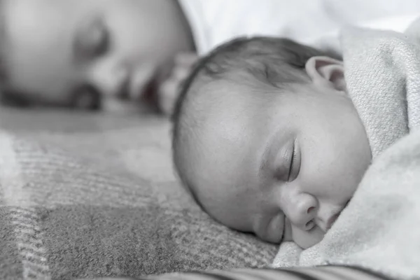 Infância, infância, família, sono, descanso, conceito de amor - preto branco perto de duas crianças, bebê recém-nascido e menina dormindo juntos em cama macia. Irmãs estão dormindo no sofá em casa . — Fotografia de Stock