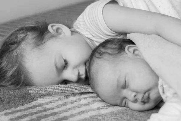 Infância, infância, família, sono, descanso, conceito de amor - preto branco perto de duas crianças, bebê recém-nascido e menina dormindo juntos em cama macia. Irmãs estão dormindo no sofá em casa . — Fotografia de Stock