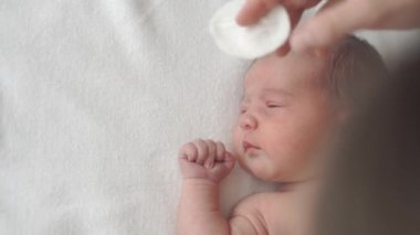 bebek bezi, çocukluk, annelik, hijyen, ilaç ve sağlık konsepti - kadın anneler yeni doğmuş çıplak bebeğin yüzünü pamuk bezle siliyor ve sırtında tıbbi klipsle klempler takıyor.