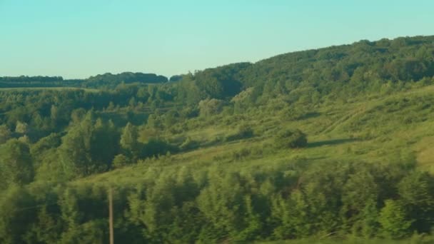 Transporte, viagem, estrada, caminho de ferro, paisagem, conceito de comnicação - visão do brilho de janela no vidro do trem de velocidade na paisagem de belos campos de natureza de prados e floresta antes do pôr do sol no verão — Vídeo de Stock