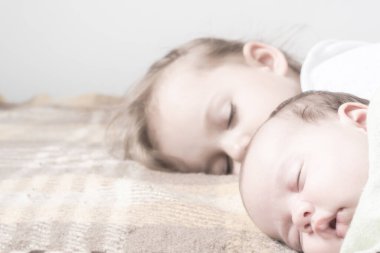 İki çocuk, yeni doğmuş bir bebek, üç yaşında bir kız bej bir yatakta yatıyor. Kardeşler evlerinde kanepede yatıyorlar. Çocukluk, bebek, aile, uyku, dinlenme, aşk konsepti. Boşluğu kopyala