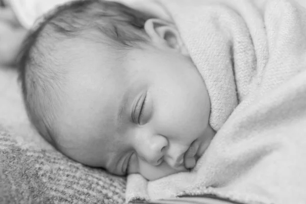 Младенчество, детство, развитие, медицина и концепция здоровья - крупным планом улыбается лицо новорожденной спящей девочки, лежащей на животе, завернутой в теплое мягкое одеяло. Черно-белое пространство — стоковое фото