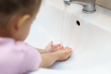 Musluğun altında sabunla ellerini suyla yıkamak. Küçük kız banyoda su ve sabunla ellerini yıkıyor. Hijyen, koronavirüs, Covid-19, karantina, çocukluk, yetiştirilme, annelik kavramı..