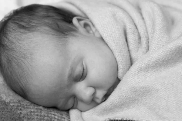 infancy, childhood, development, medicine and health concept - close-up smiling face of newborn sleeping baby girl lying on stomach covered wrapped in warm soft blanket. Black and white Copy space